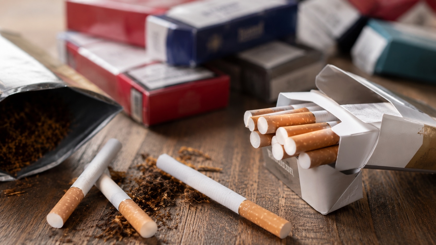 Cigarettes, tabac à rouler et paquets ouverts posés sur une table en bois.