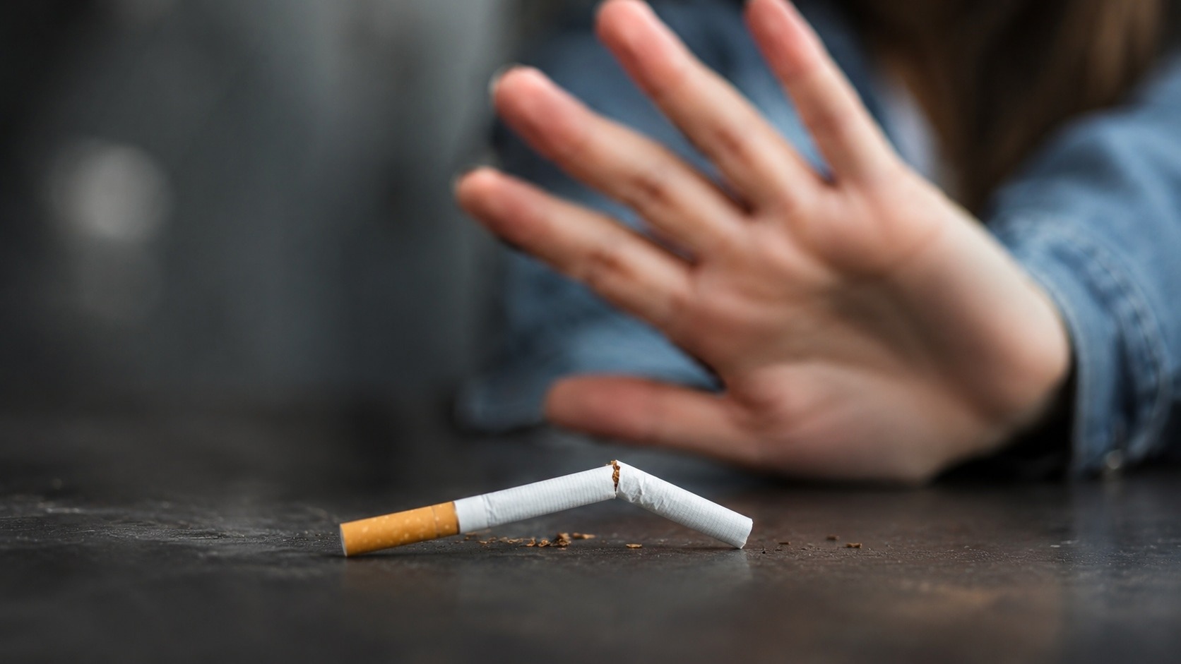 Une cigarette cassée en deux posée sur une table, devant une main qui la repousse.