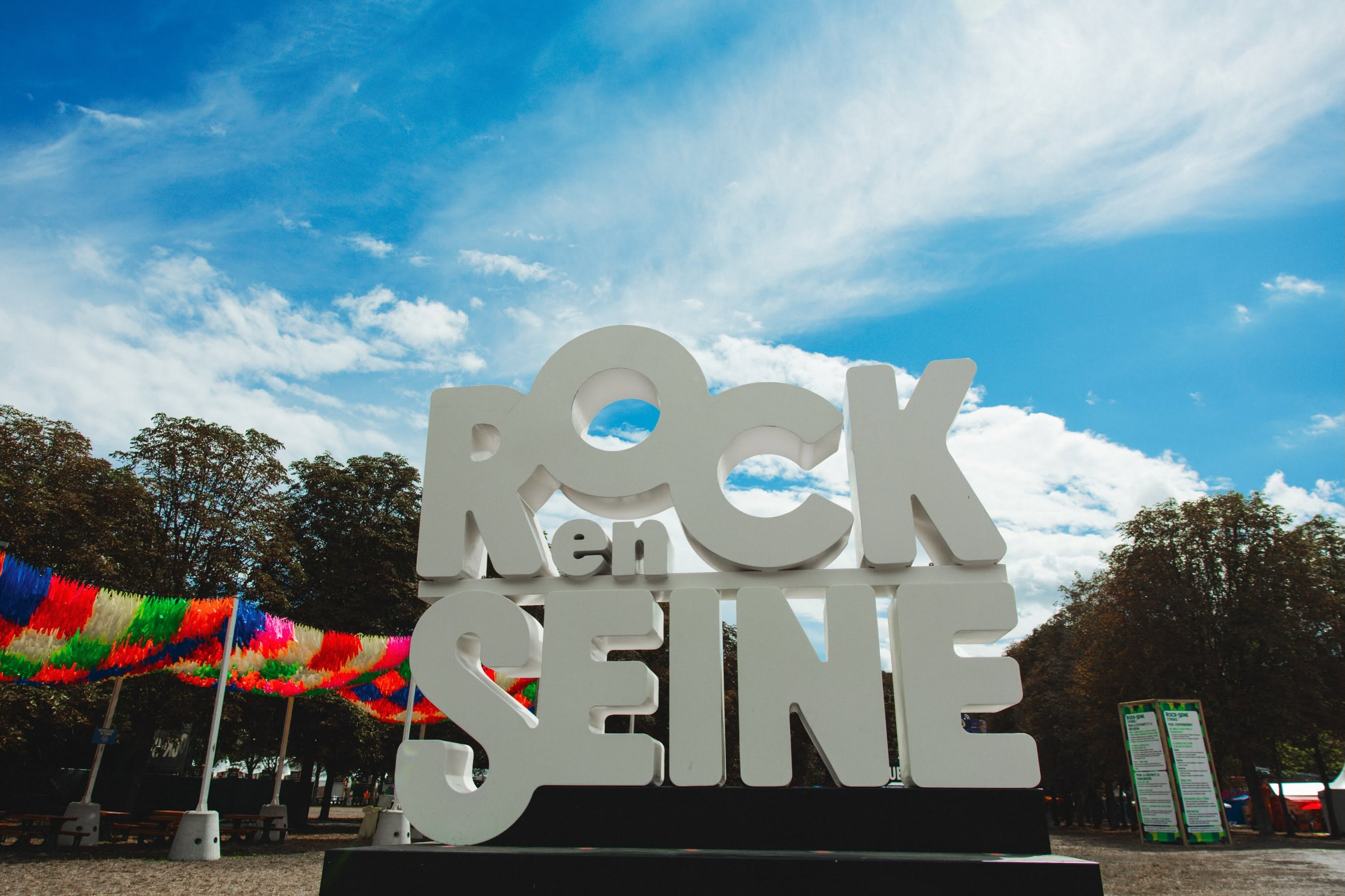 Lettres blanches Rock en Seine installées au sol, avec les arbres du parc de Saint-Cloud en arrière-plan.